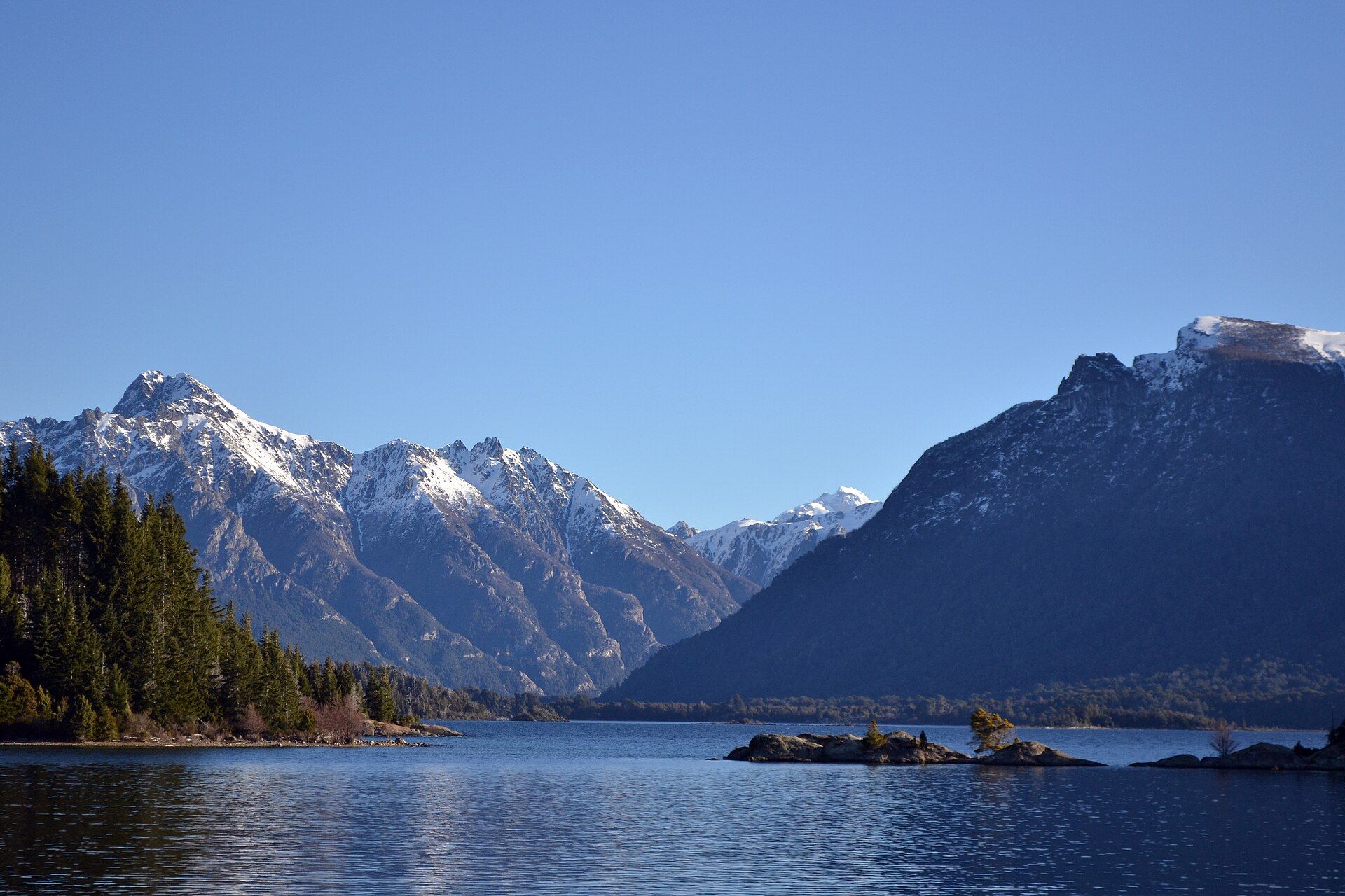 Lake Nahuel Huapi in early light, with a wooded shore in front and the snow-covered Andes across the water