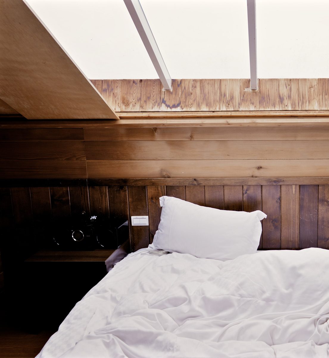 An attic bedroom lined in cypress boards, with a long skylight above the bed and white linen turned down
